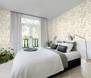 Papel mural non-woven lavable para interiores con un diseño de hojas delicadas en tonos gris y café, con efecto acuarela, instalado en dormitorio